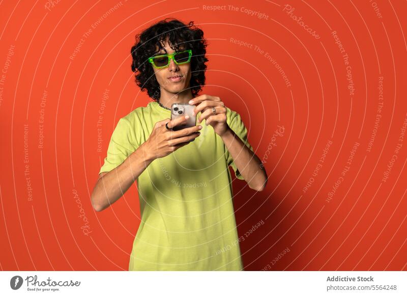 Junger ethnischer Mann schreibt eine SMS auf seinem Smartphone Sonnenbrille benutzend männlich jung stehen Lateinamerikaner hispanisch Textnachricht Mobile