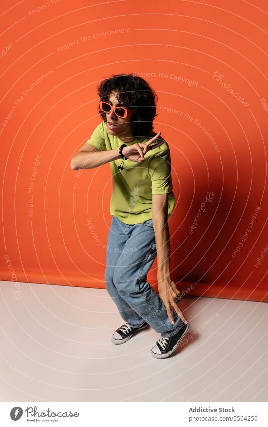 Junger ethnischer Mann tanzt mit Sonnenbrille in der Nähe der roten Wand Tänzer aufgeregt expressiv flippig Spaß haben Tanzen genießen männlich jung stehen