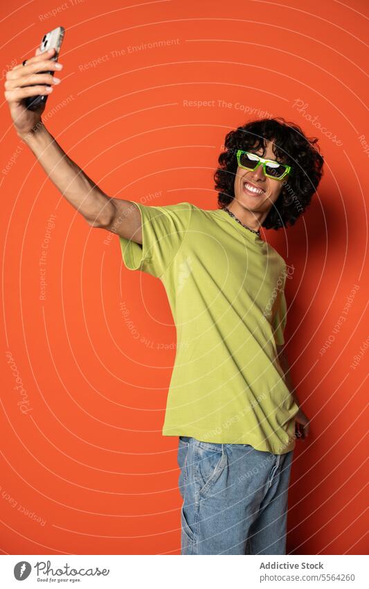 Glücklicher junger ethnischer Mann macht Selfie mit Smartphone Sonnenbrille Lächeln benutzend positiv heiter männlich stehen Lateinamerikaner hispanisch Mobile