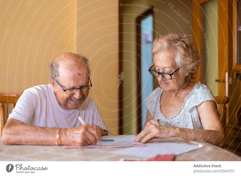 Großeltern machen Gedächtnisübungen zu Hause Großvater Großmutter Brille sitzen Tisch Stuhl üben Übung Fokus Konzentration Arbeit herabsehend heimwärts