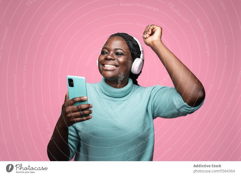 Entzückte afrikanische Frau mit Smartphone und rosa Kopfhörern Afrikanisch Lächeln blaugrün Freude hören Hintergrund Ausdruck Emotion Tanzen Schwingung Riffel