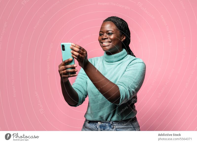 Fröhliche afrikanische Frau telefoniert vor rosa Hintergrund Afrikanisch Smartphone türkis Rollkragenpulli blaugrün erfassend Moment freudig Lächeln