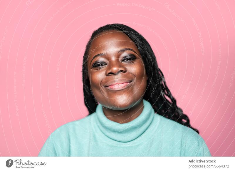 Porträt einer fröhlichen afrikanischen Frau vor rosa Hintergrund Afrikanisch Lächeln Freude blaugrün Pullover Glück Gesicht Schönheit Emotion Zähne Ausdruck
