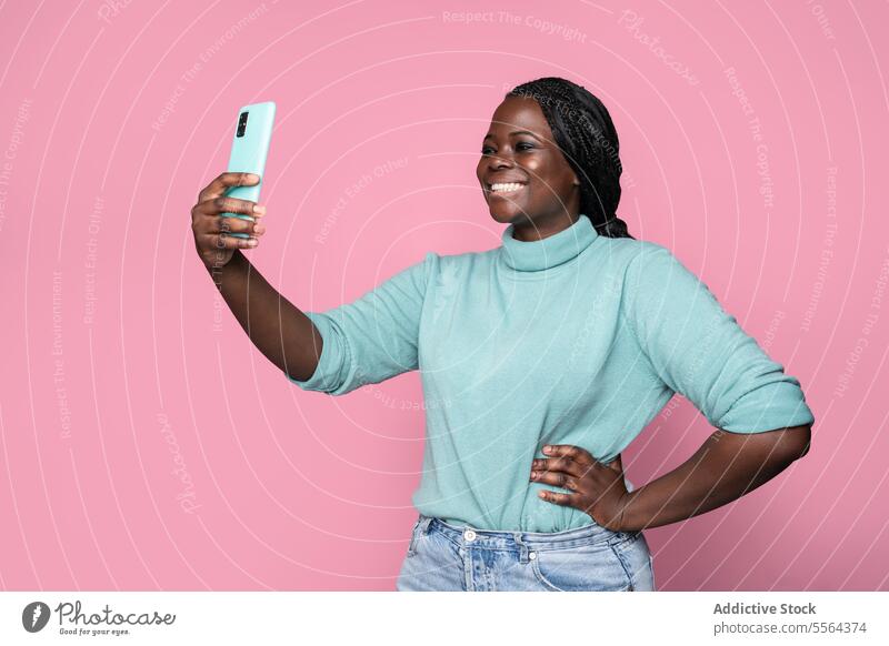 Afrikanische Frau macht Selfie mit Smartphone vor rosa Hintergrund blaugrün Rollkragenpulli türkis Freude Stil Mode Porträt Technik & Technologie Mobile heiter
