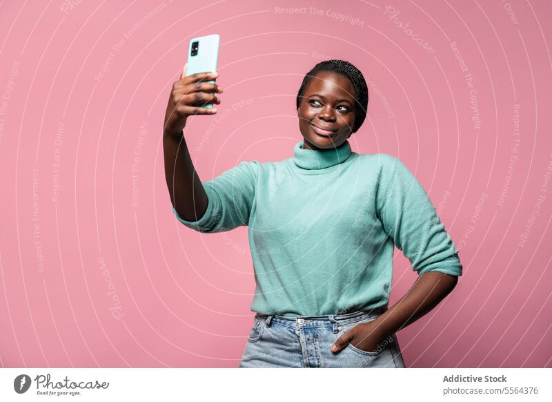 Afrikanische Frau nimmt Selfie gegen rosa Hintergrund Smartphone blaugrün Pullover Pose einfangen Freude Foto Mobile Fotokamera Spaß Gedächtnis Lifestyle Moment