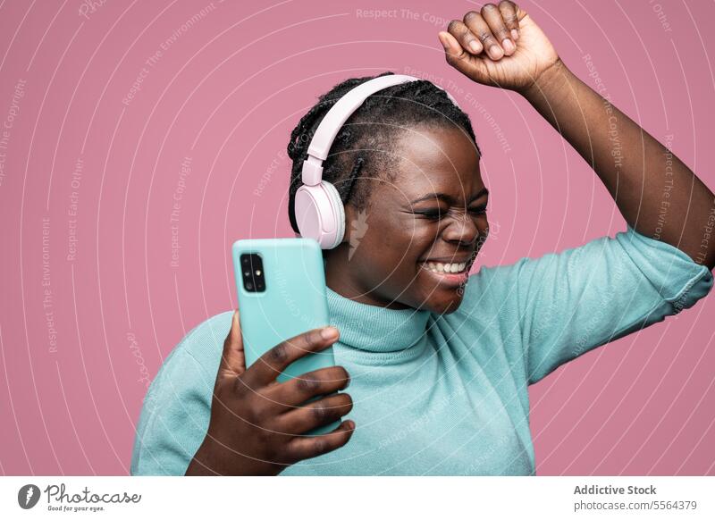 Afrikanische Frau genießt Musik mit Kopfhörern und Smartphone rosa blaugrün Freude hören Hintergrund Ausdruck Emotion Tanzen Schwingung Riffel Stimmung