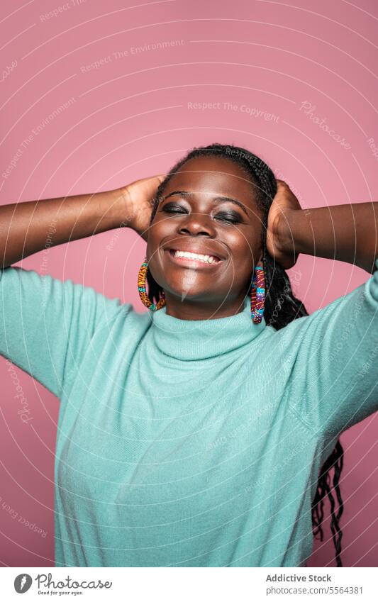 Porträt einer lächelnden afrikanischen Frau mit Zöpfen Afrikanisch Lächeln freudig Fröhlichkeit geflochten Behaarung Ohrringe farbenfroh türkis Pullover rosa
