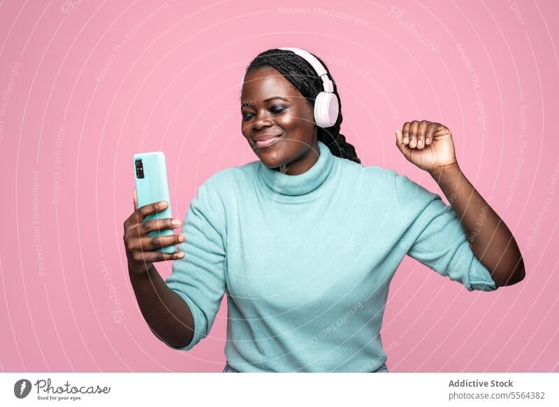Afrikanische Frau genießt Musik vor einem rosa Hintergrund Tanzen Freude Smartphone Kopfhörer Rhythmus Spaß Bewegung Riffel Fröhlichkeit Entertainment Freizeit
