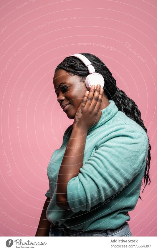 Gelassene afrikanische Frau genießt Musik Afrikanisch Kopfhörer rosa Hintergrund Gelassenheit zuhören Seite Ansicht Windstille friedlich Emotion