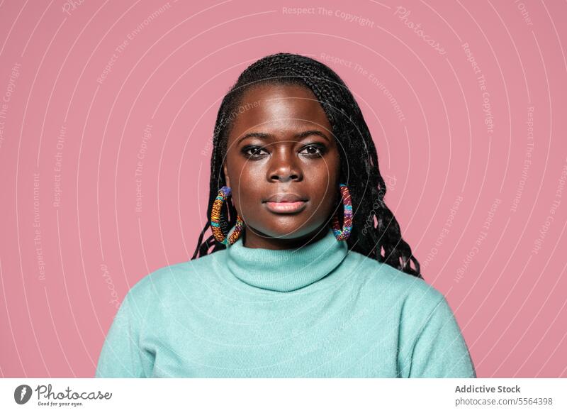 Afrikanische Frau in türkisfarbenem Rollkragenpullover Porträt geflochten Behaarung farbenfroh Ohrringe Rollkragenpulli rosa Hintergrund Schönheit Mode Stil