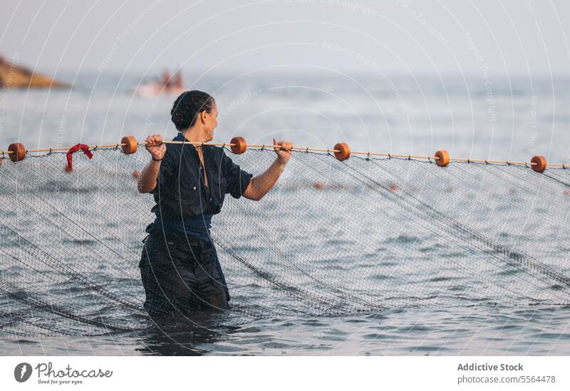 Glückliche junge Frau in der Nähe von Fischernetz im Wasser bei Tageslicht stehend Fischen Netz Lächeln MEER Seil Meer nass Sommer tagsüber Sonne Natur positiv