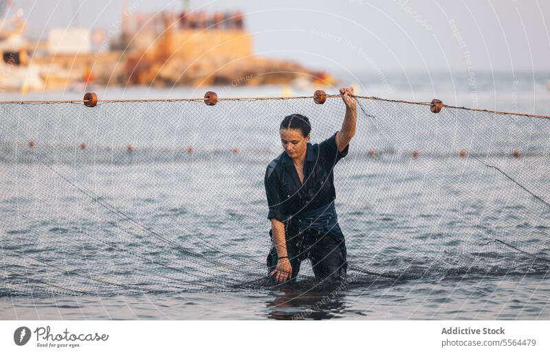 Ernste junge Frau steht bei Tageslicht in der Nähe eines Fischernetzes im Wasser Fischen Netz MEER Seil Meer nass Sommer tagsüber Sonne Natur positiv