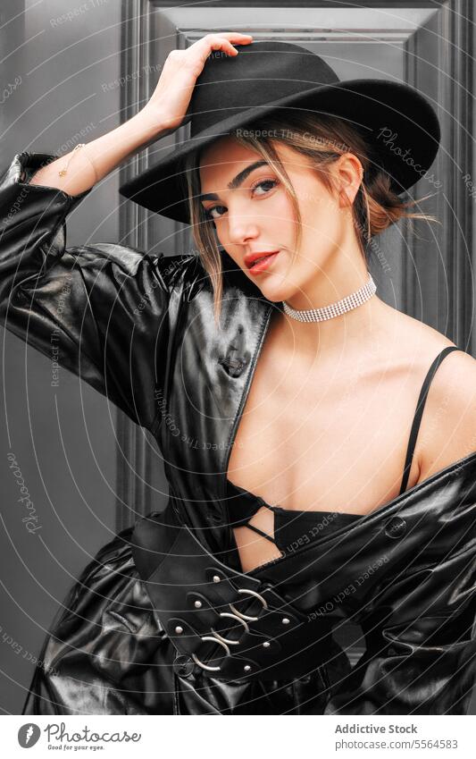 Porträt einer jungen stilvollen kaukasischen Frau in einem schwarzen Ledermantel und Hut, die in die Kamera schaut. Kaukasier Mädchen Model