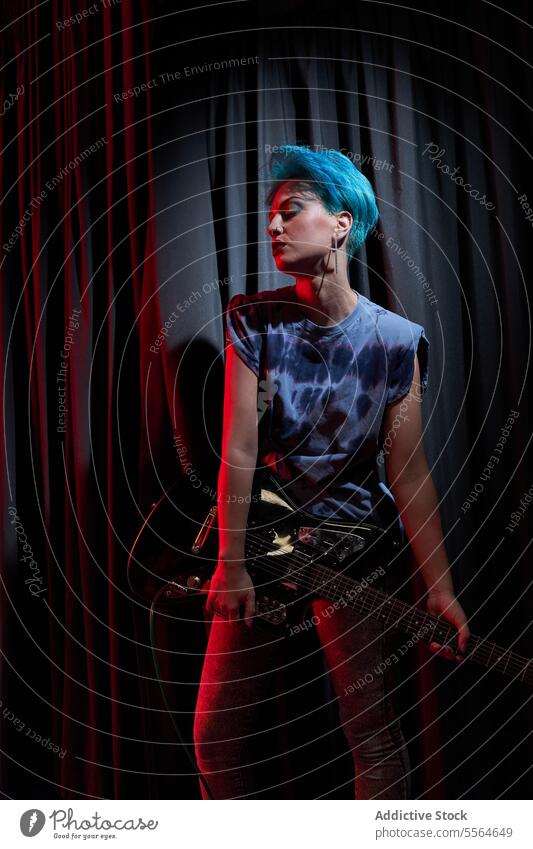Junge stilvolle Frau mit E-Gitarre in den Händen in einem dunklen Raum Musiker führen ernst Gitarrenspieler Instrument ausführen Schauplatz gefärbtes Haar jung