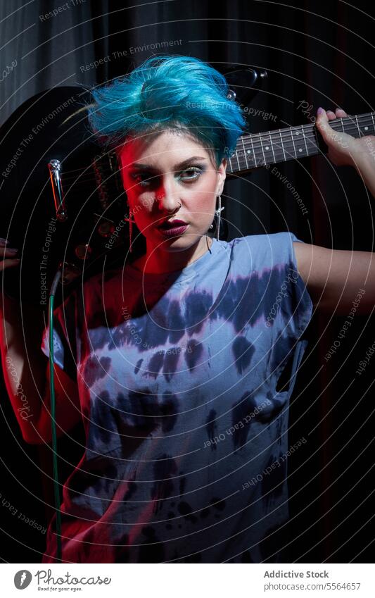 Junge stilvolle Frau trägt E-Gitarre hinter dem Kopf in einem dunklen Raum Musiker führen ernst Gitarrenspieler Instrument ausführen Schauplatz Porträt
