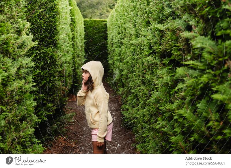 Preteen-Mädchen im Kapuzenpulli steht in der Nähe von grünen Bäumen Kind nadelhaltig Park Baum Straße besinnlich nachdenklich Landschaft stehen Natur Irrgarten