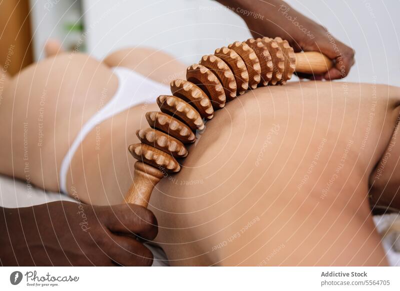 Crop-Masseur massiert den Rücken einer nicht erkennbaren Kundin mit einem Holzinstrument im Salon Massage Schulter Rolle Verfahren Leckerbissen Therapie