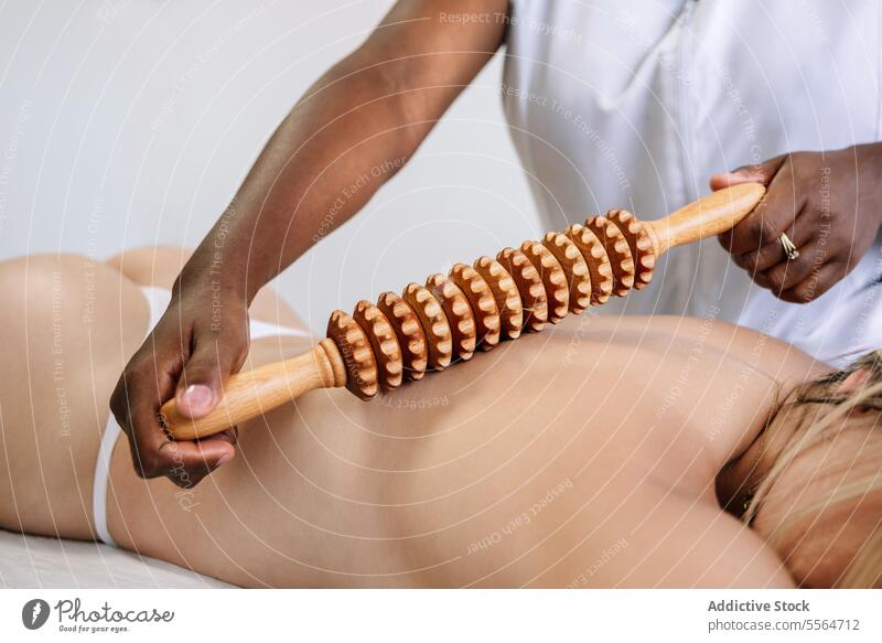 Crop-Masseur massiert den Rücken einer nicht erkennbaren Kundin mit einem Holzinstrument im Salon Massage Schulter Rolle Verfahren Leckerbissen Therapie