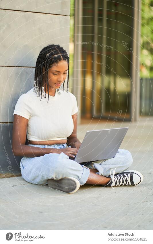 Fokussierte afroamerikanische Frau, die einen Laptop benutzt, während sie auf dem Boden sitzt Arbeit freiberuflich benutzend online Surfen Internet pc Browsen