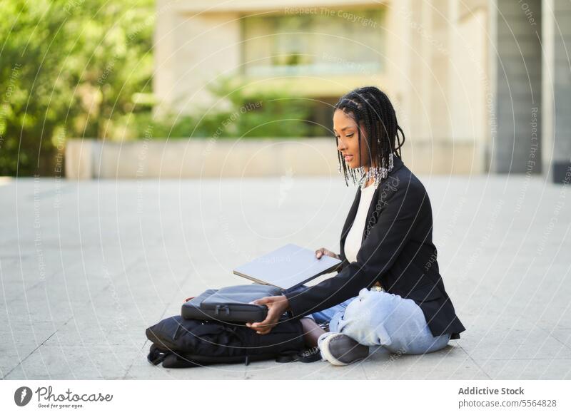 Afroamerikanische Frau sitzt mit Laptop auf dem Boden vor einem unscharfen Hintergrund eines Gebäudes Straße Geschäftsfrau modern Arbeit Netbook Unternehmer
