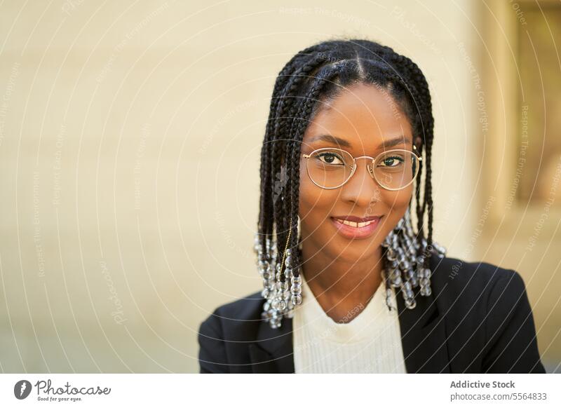 Lächelnde stilvolle afroamerikanische Frau vor einem unscharfen Hintergrund Stil Geschäftsfrau selbstbewusst Outfit Gebäude urban modern positiv Unternehmer