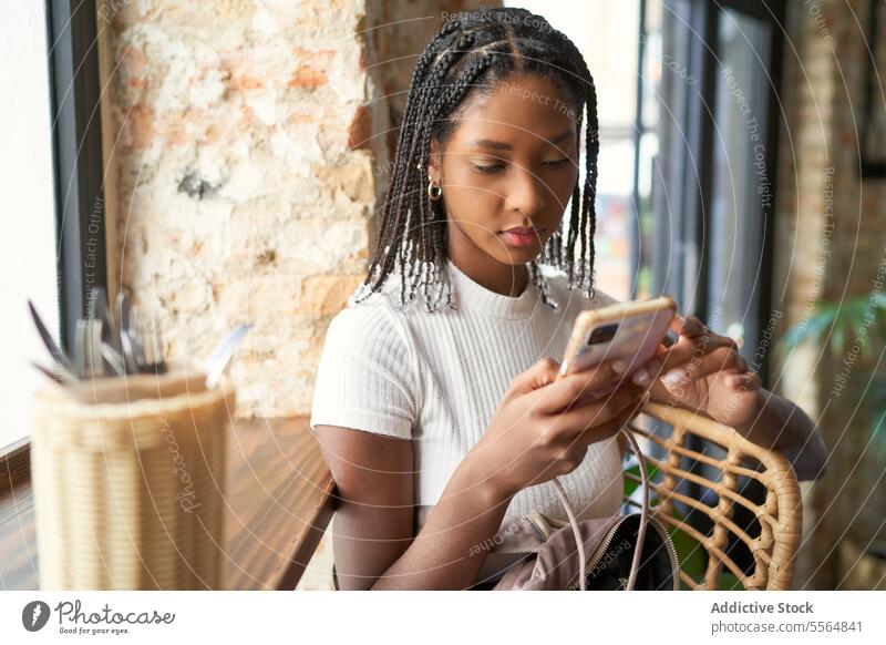 Fokussierte afroamerikanische Frau mit Afrozöpfen, die ein Smartphone benutzt benutzend Browsen besinnlich Konzentration alt schäbig Surfen Mobile Telefon
