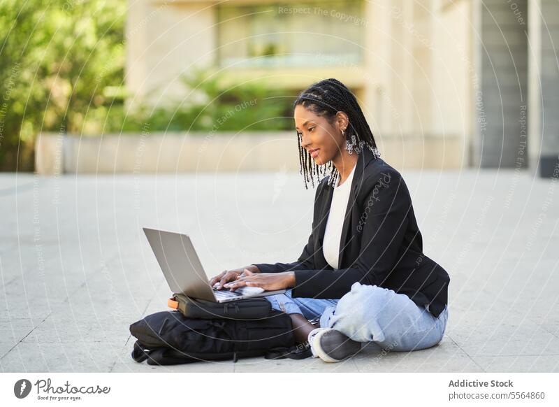 Afroamerikanische Frau sitzt mit Laptop auf dem Boden vor einem unscharfen Hintergrund eines Gebäudes Straße Geschäftsfrau modern Arbeit Netbook Unternehmer