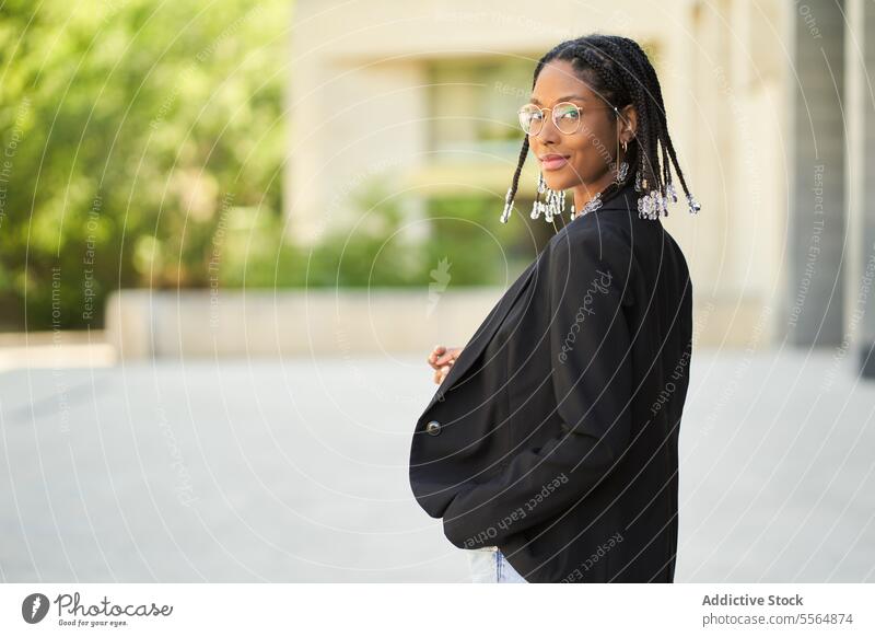 Lächelnde stilvolle afroamerikanische Frau vor einem unscharfen Hintergrund Stil Geschäftsfrau selbstbewusst Outfit Gebäude urban modern positiv Unternehmer