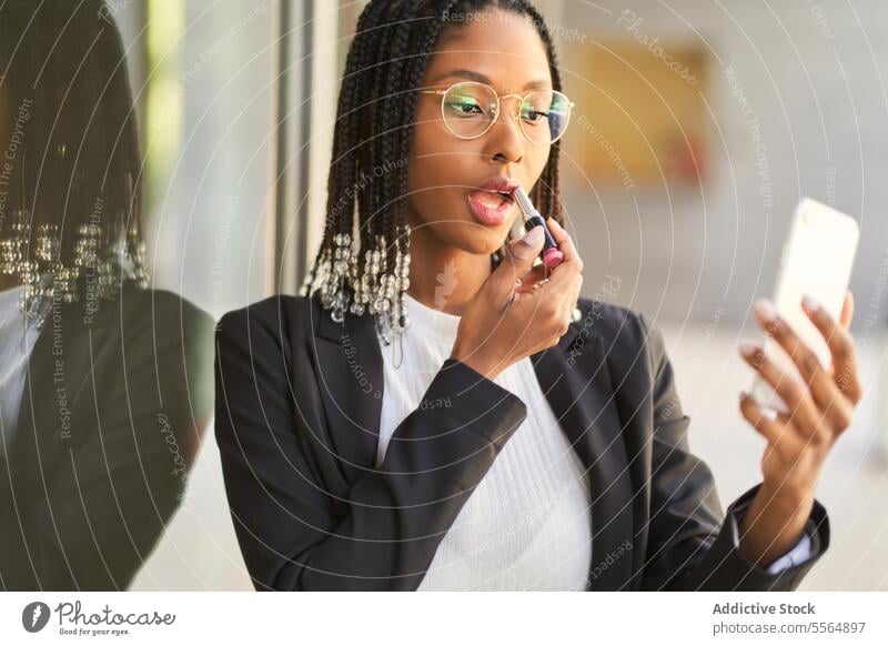 Schwarze Geschäftsfrau benutzt Smartphone als Spiegel beim Schminken Frau benutzend Lippenstift Make-up Unternehmer Reflexion & Spiegelung Tun Zopf Frisur