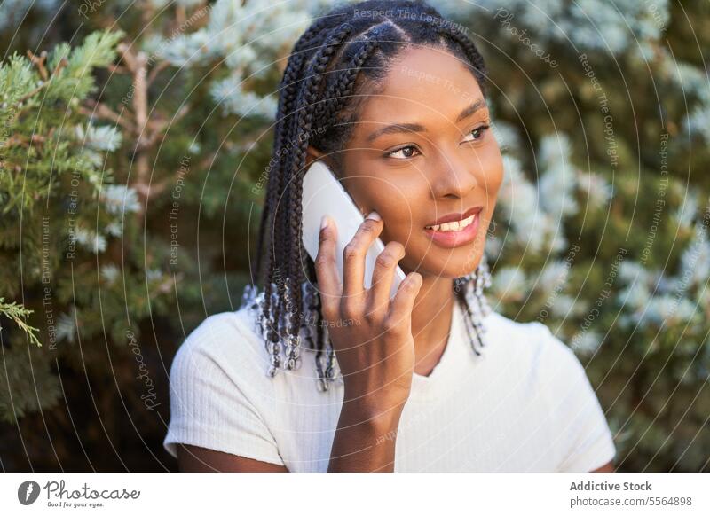 Erfreute afroamerikanische Frau, die im Garten mit ihrem Smartphone spricht Lächeln positiv Gespräch sprechen reden Telefonanruf Park Mobile lässig Funktelefon