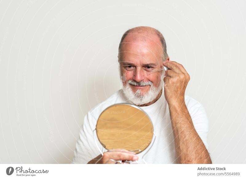 Älterer Mann hält Spiegel und trägt Serum auf Gesicht auf ätherisches Öl verjüngen Anti-Aging Kosmetologie Hautfalten Gesichtsbehandlung Kosmetik männlich