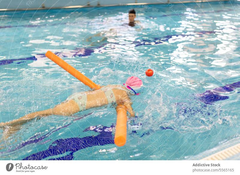 Mädchen im Vorschulalter übt Schwimmen unter Aufsicht eines Schwimmlehrers Pool im Innenbereich Schwimmer Vorschulkind Nudel orange Ausbilderin Sicherheit