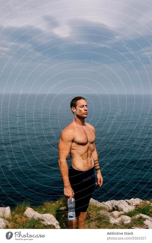 Mann stehend am Meer mit Wasserflasche MEER getönt Physis Himmel Wolken Horizont Fitness Gesundheit Natur im Freien Training Hydratation Muskeln Gelassenheit