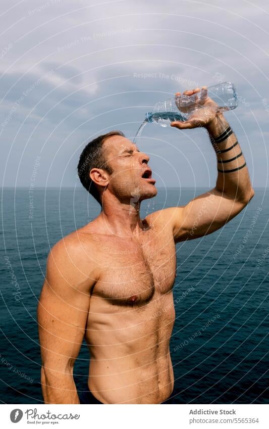 Mann erfrischt sich mit Wasser mit Ozean Hintergrund. erfrischend Meer Himmel wolkig platschen Gesicht Stehen Fitness Hydrat durstig Wellness Sommer erwärmen