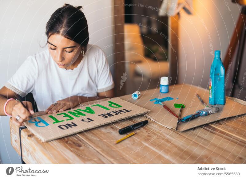Frau malt ein Plakat über die Umwelt Farbe Text Erde Karton Tisch Kunst Raum gemütlich Proviant Design Bürste heimwärts Holz sitzen Freude Kreativität