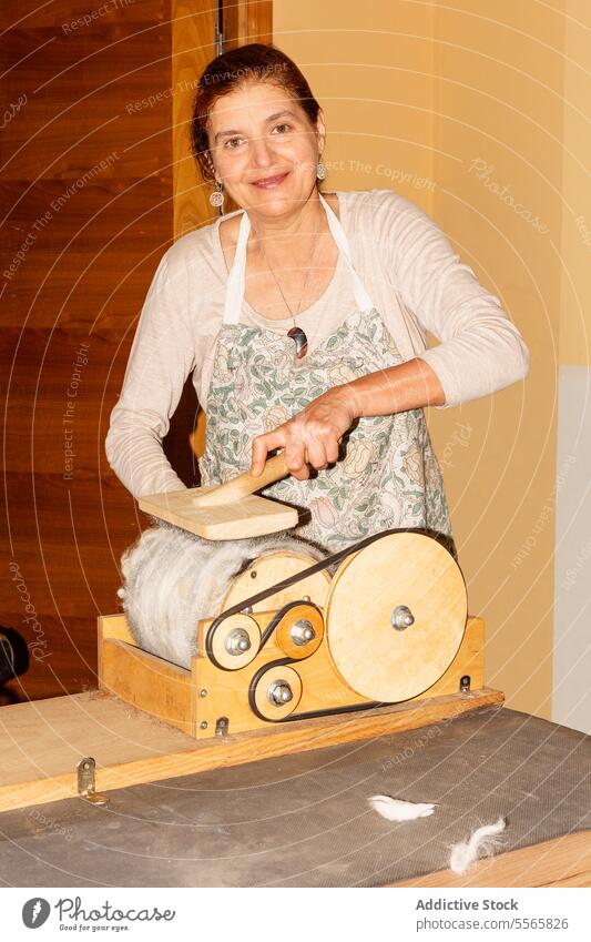 Titel: Frau bereitet Wolle mit Trommelkarder in hellem Raum vor Vorbereitung Spinning handbetrieben Lächeln Arbeit Textil Sehne Handwerk Gerät Werkzeug manuell