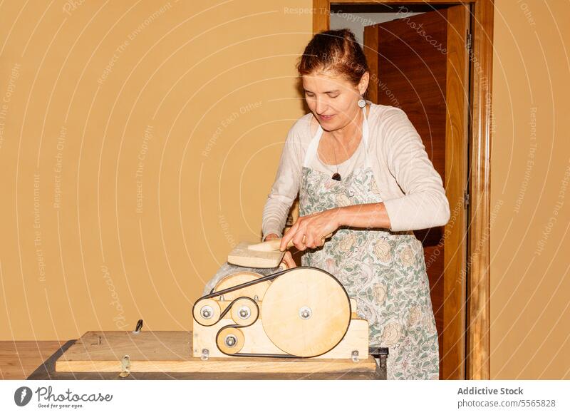 Titel: Frau bereitet Wolle mit Trommelkarder in hellem Raum vor Vorbereitung Spinning handbetrieben Lächeln Arbeit Textil Sehne Handwerk Gerät Werkzeug manuell
