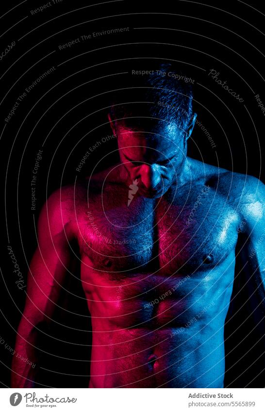 Hemdloser muskulöser Mann in dunklem Raum mit Neonbeleuchtung Studioaufnahme stark ohne Hemd nackter Torso neonfarbig dunkel Körper glühen Windstille Energie