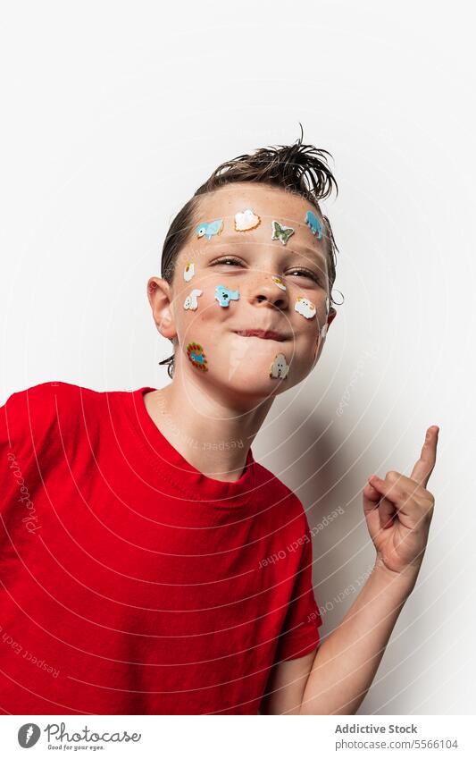 Junge mit Tieraufklebern im Gesicht Aufkleber nasses Haar rotes Hemd weißer Hintergrund Kind spielerisch Spaß Porträt Nahaufnahme Ausdruck niedlich Jugend