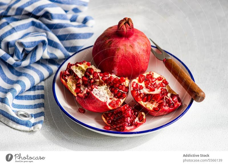 Öffnen Sie den reifen Granatapfel auf dem Teller mit einem rustikalen Messer und einer gestreiften Serviette. Samen Frucht rot pulsierend frisch Stoff Textur