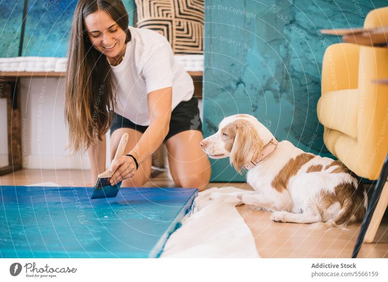 Junge Künstlerin malt auf Holzbrett mit Pinsel neben Hund Frau Farbe Pinselblume zeichnen Haustier Werkstatt Anstreicher Staffelei Fähigkeit kreativ Kunst Fokus