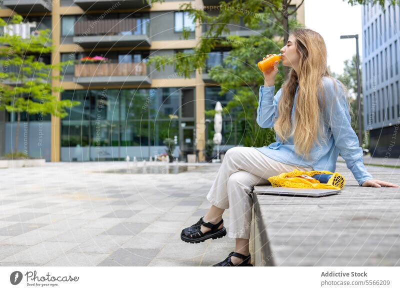 Studentin nippt in der Mittagspause in der Stadt an einem Getränk im Freien. Schüler blond Frau jung Gen-Z trinken Zahnspange Sitzen Saft Kaukasier blaues Hemd