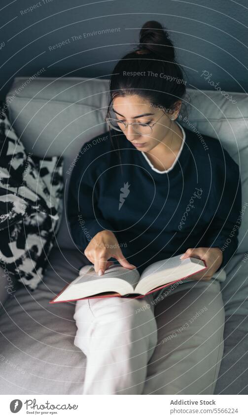 Junge Frau sitzt auf dem Sofa und liest ein Buch im Tageslicht lesen lernen Etage sich[Akk] entspannen Komfort Zeitvertreib Wohnzimmer zu Hause jung Freizeit