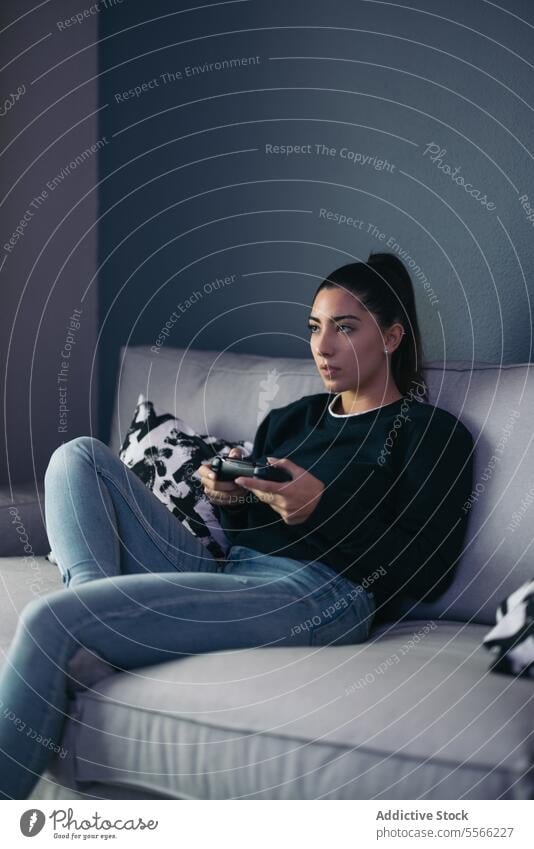 Positive Frau, die zu Hause ein Videospiel mit Joystick spielt spielen Konsole Spiel Sofa benutzend Apparatur Gerät heimwärts Wohnzimmer Gamepad lässig Freizeit