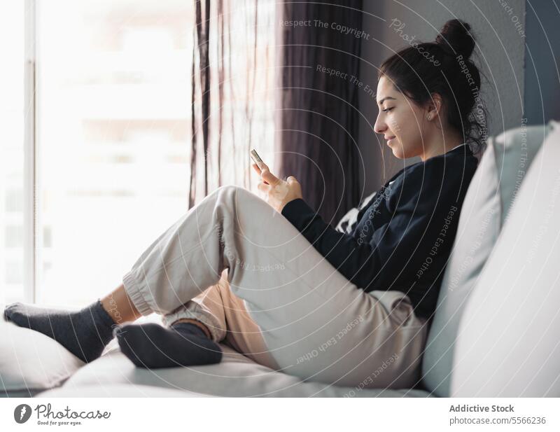Glückliche junge Frau mit Smartphone auf dem Sofa liegend benutzend Nachricht sich[Akk] entspannen online Internet Lächeln Wohnzimmer sitzen Browsen Surfen