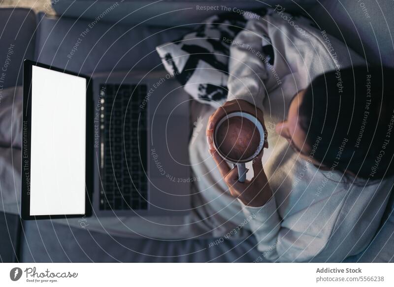Unkenntlich gemachte junge Frau mit Laptop und Kaffeetasse Tasse benutzend Internet Anschluss online Wohnzimmer zu Hause dunkles Haar leerer Bildschirm Sofa