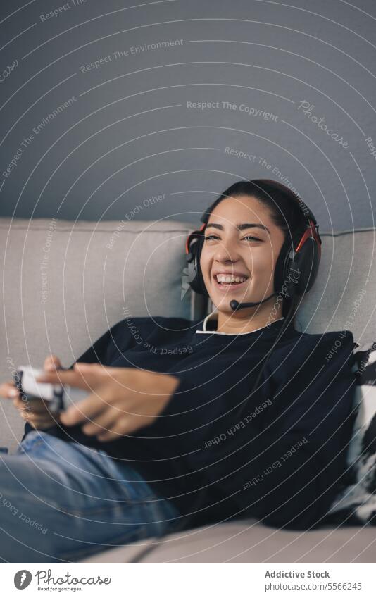 Lächelnde Frau, die zu Hause ein Videospiel mit einem Controller spielt Lachen spielen Joystick Spieler Sofa heiter benutzend Konsole unterhalten Kopfhörer
