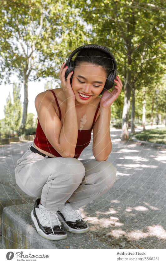 Asiatische Frau genießt Musik im Park Kopfhörer Freude hören Bäume Natur Lächeln sonnig Tag Outfit Sommer Erholung im Freien Freizeit Fröhlichkeit Stil