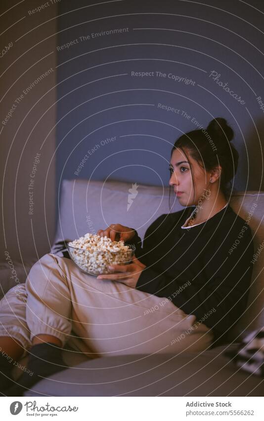 Junge Frau, die sich auf einem bequemen Sofa mit Popcornschüssel im Wohnzimmer ausruht Popkorn sich[Akk] entspannen Komfort Schalen & Schüsseln Kniestrümpfe