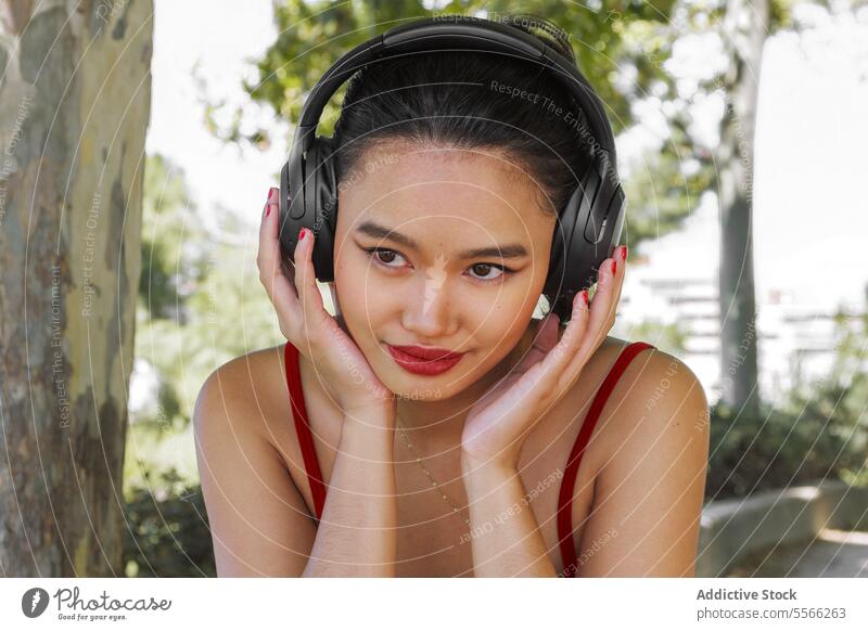 Asiatische Frau genießt Musik im Park Kopfhörer Freude hören Bäume Natur Lächeln sonnig Tag Outfit Sommer Erholung im Freien Freizeit Fröhlichkeit Stil